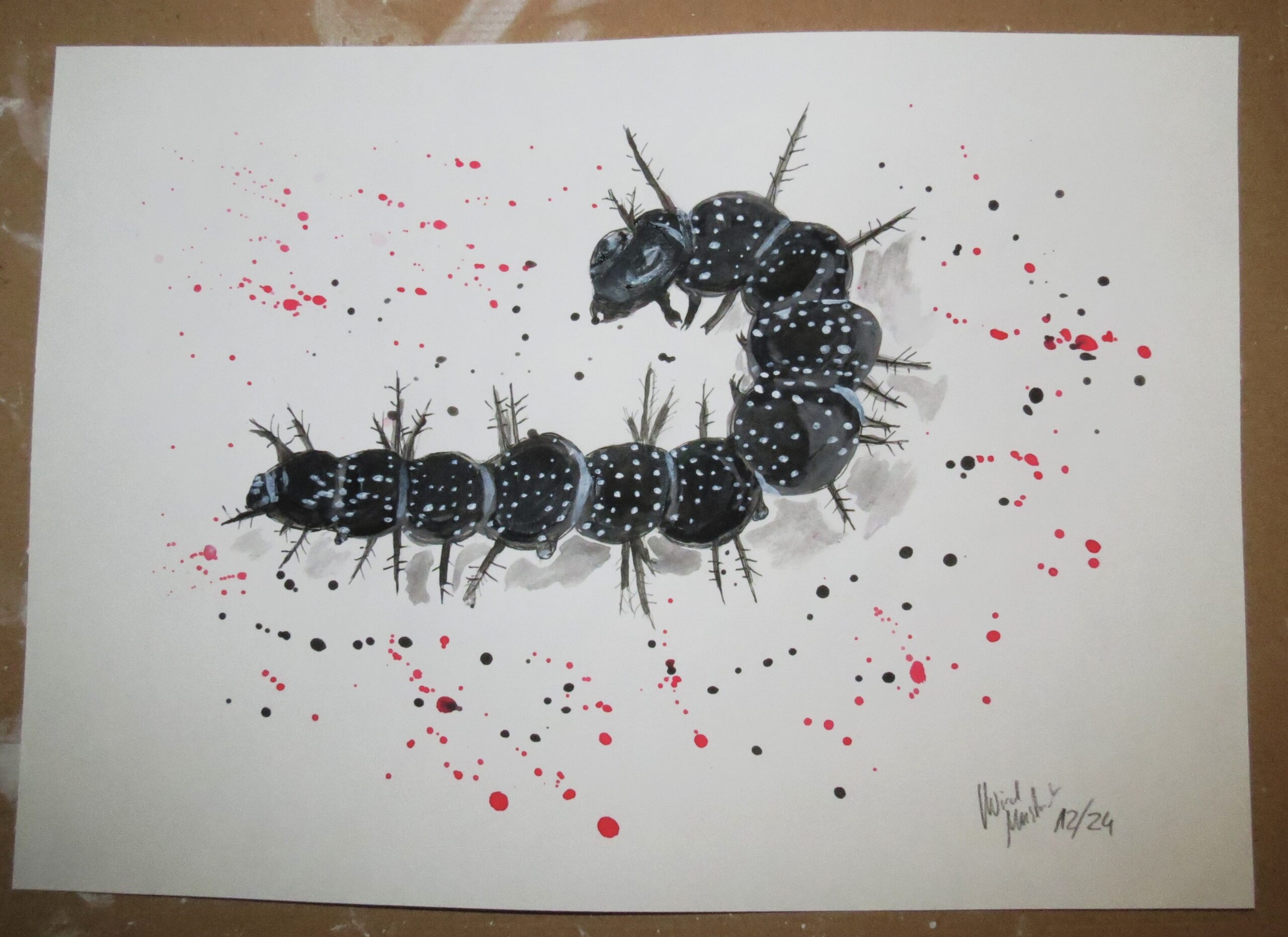 a very thorny black and darkblue caterpillar on paper speckled with black and red color splashes